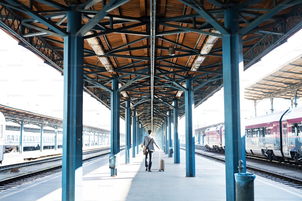 Bello uomo d'affari maturo in una città. Uomo che cammina sulla piattaforma ferroviaria sulla stazione ferroviaria. Veduta posteriore.
