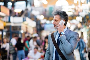 Handsome mature businessman with smartphone in a city, making a phone call. Blurred background.