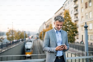 Handsome mature businessman with a smartphone in a city, texting.