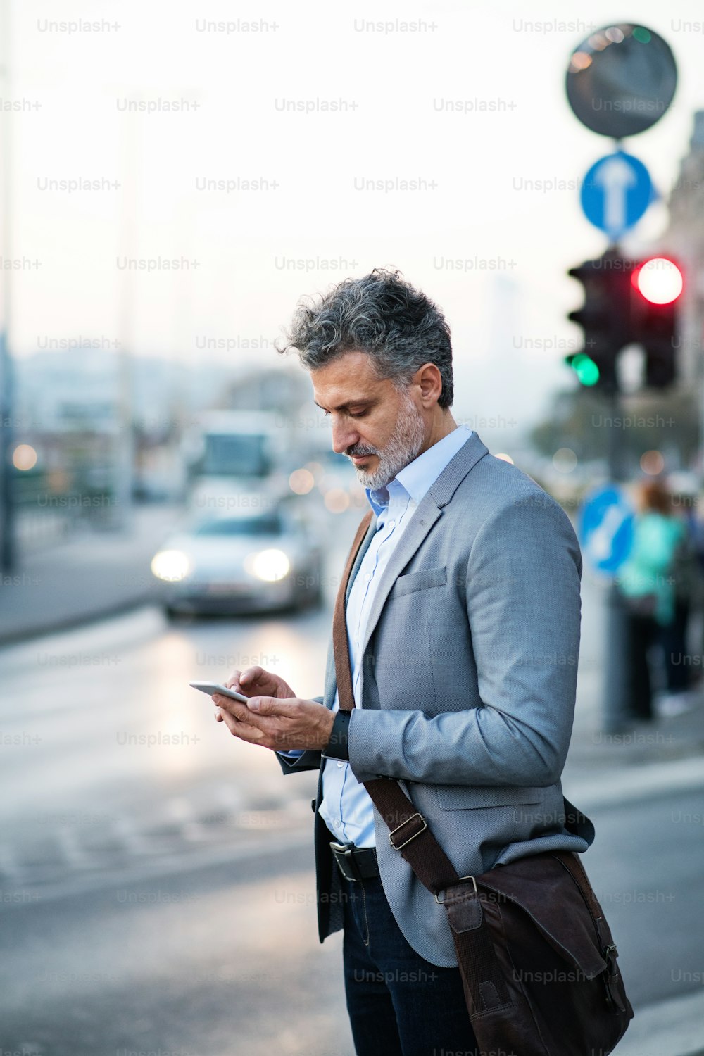 Handsome mature businessman with smartphone in a city, text messaging.