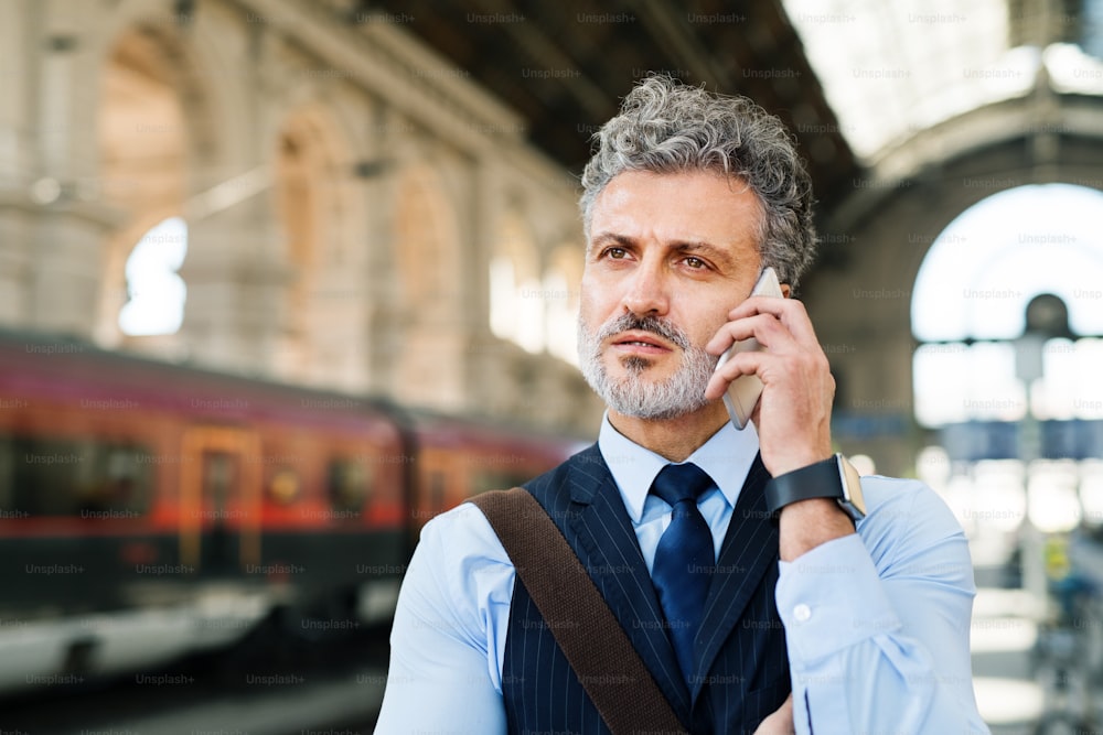 Handsome mature businessman with smartphone in a city. Man waiting for the train at the railway station, making a phone call.