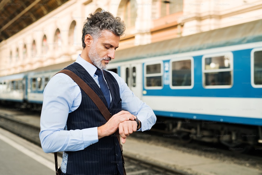 Handsome mature businessman in a city. Man waiting for the train at the railway station, checking times.