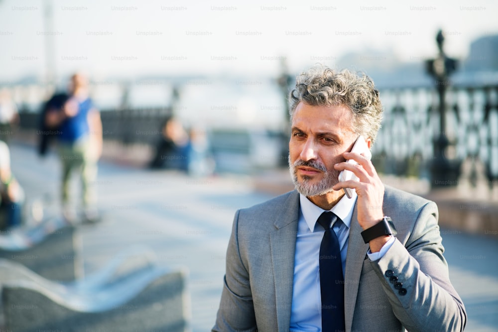 Bel homme d’affaires mature avec smartphone dans une ville. Homme faisant un appel téléphonique.