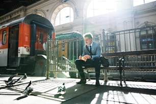 Handsome mature businessman in a city. A man waiting for the train at the railway station. A man sitting on a bench, feeding pigeons.