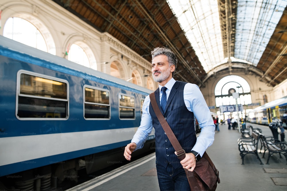 Bel homme d’affaires mature dans une ville. Homme attendant le train à la gare, marchant.