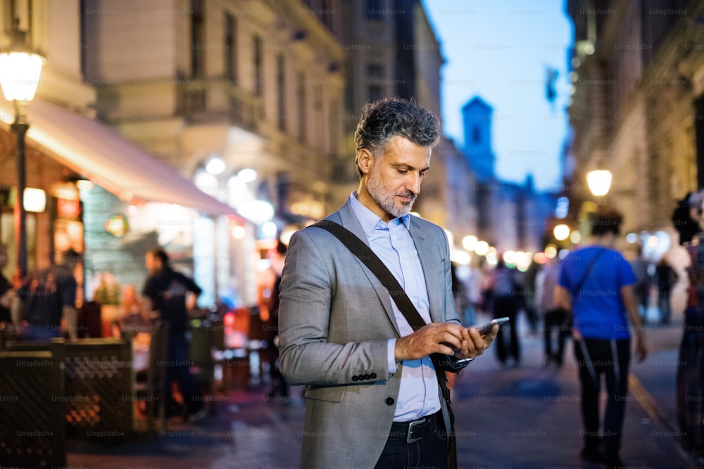 Empresário bonito e maduro com um smartphone em uma cidade, enviando mensagens de texto.