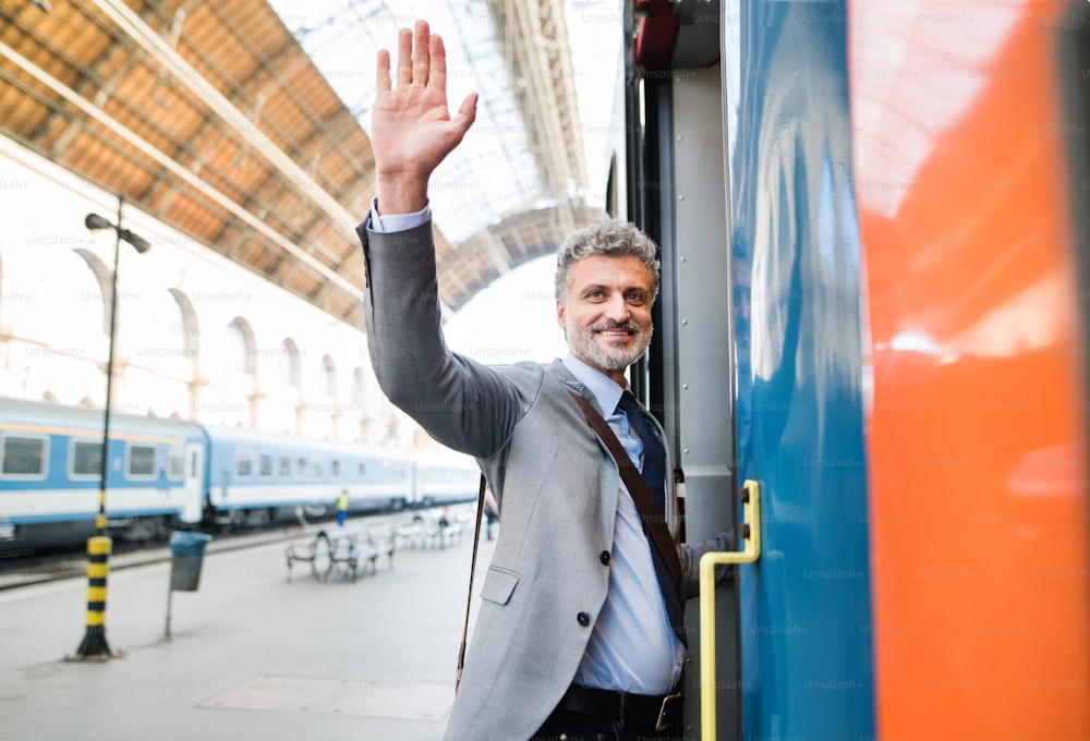 Bel homme d’affaires mature dans une ville. Homme montant dans le train à la gare en faisant signe.