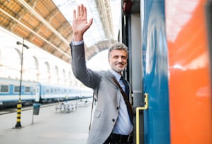 Bello uomo d'affari maturo in una città. Uomo che sale sul treno alla stazione ferroviaria, salutando.