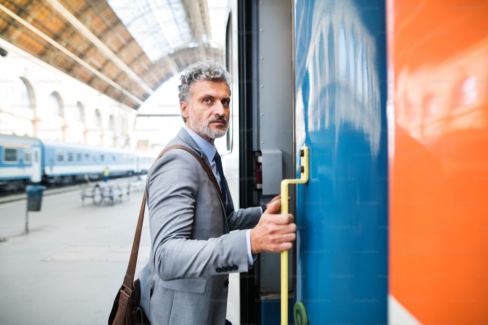 Handsome mature businessman in a city. Man getting on the train at the railway station.