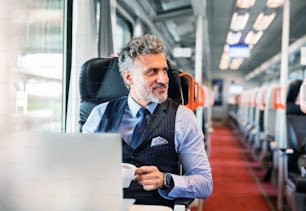 Handsome mature businessman travelling by train. A man with laptop and a coffee.