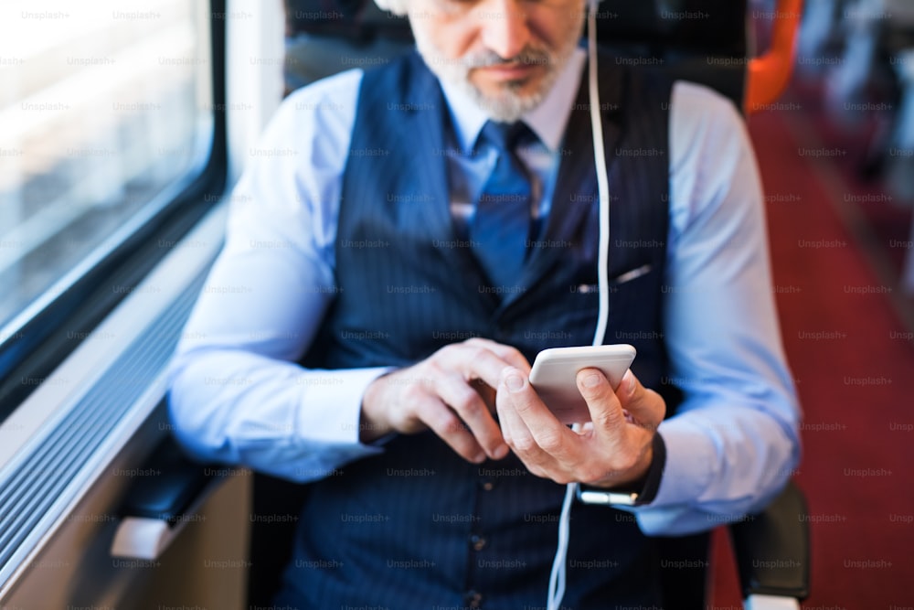 Unrecognizable mature businessman travelling by train. A man with smartphone and headphones, listening to music.