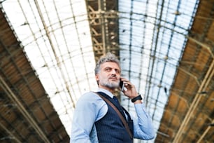 Bello uomo d'affari maturo con smartphone in una città. Uomo in attesa del treno alla stazione ferroviaria, facendo una telefonata.
