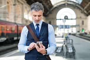 도시에서 스마트폰을 가진 잘생긴 성숙한 사업가. 기차역에서 기차를 기다리는 남자, 문자 메시지.