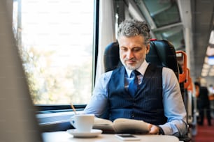 Handsome mature businessman travelling by train, reading a book.