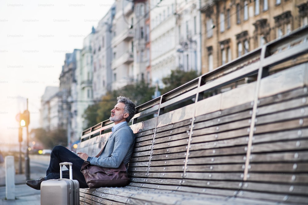 Gutaussehender reifer Geschäftsmann in einer Stadt, der auf einer Bank sitzt und wartet.