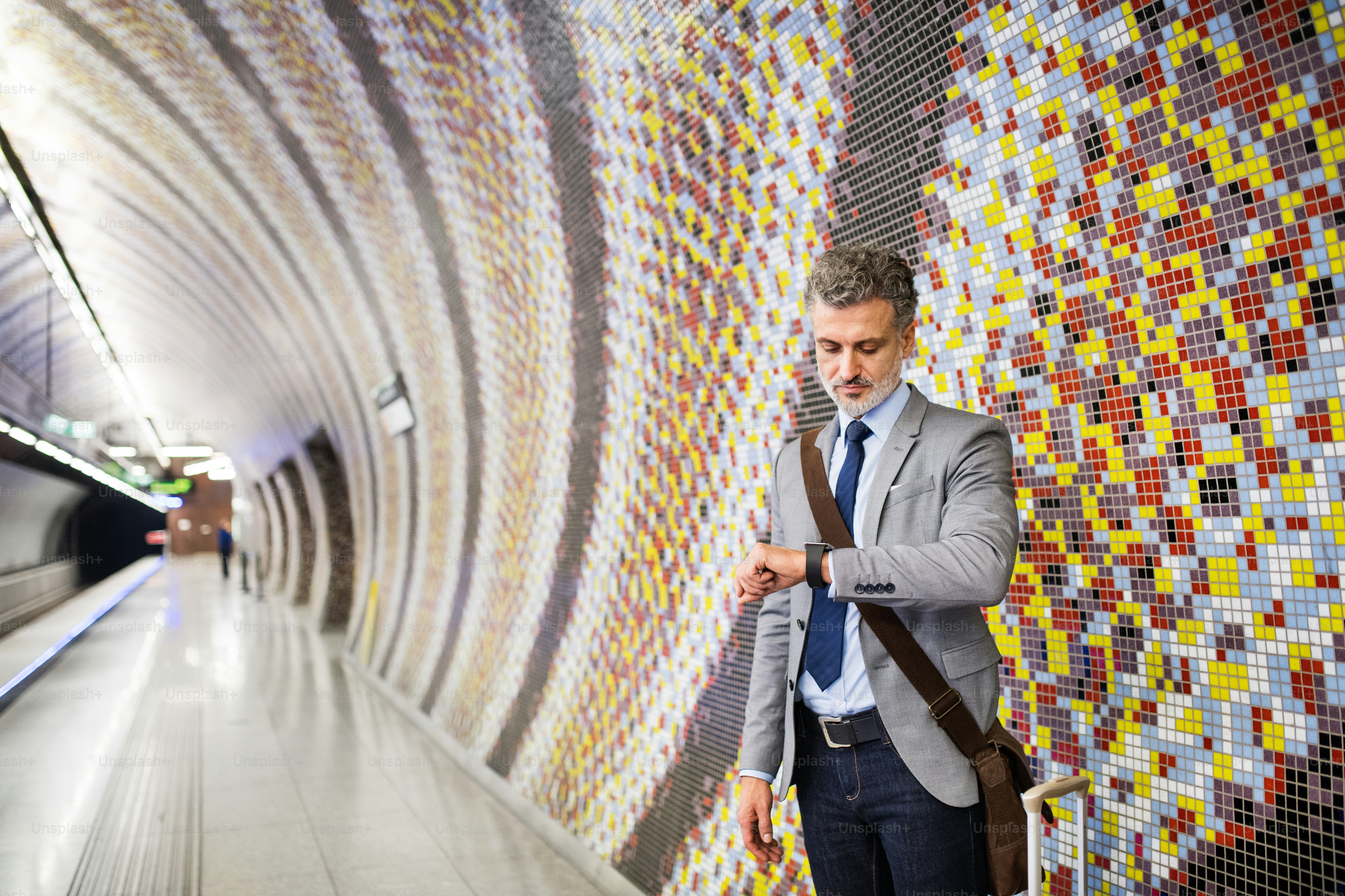 Handsome mature businessman in a city. Man waiting for the train at the subway station, checking times