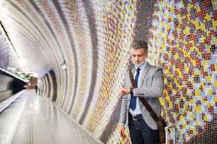 Handsome mature businessman in a city. Man waiting for the train at the subway station, checking times.