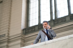 Handsome mature businessman with smartphone in a city. Man at the railway station, making a phone call.