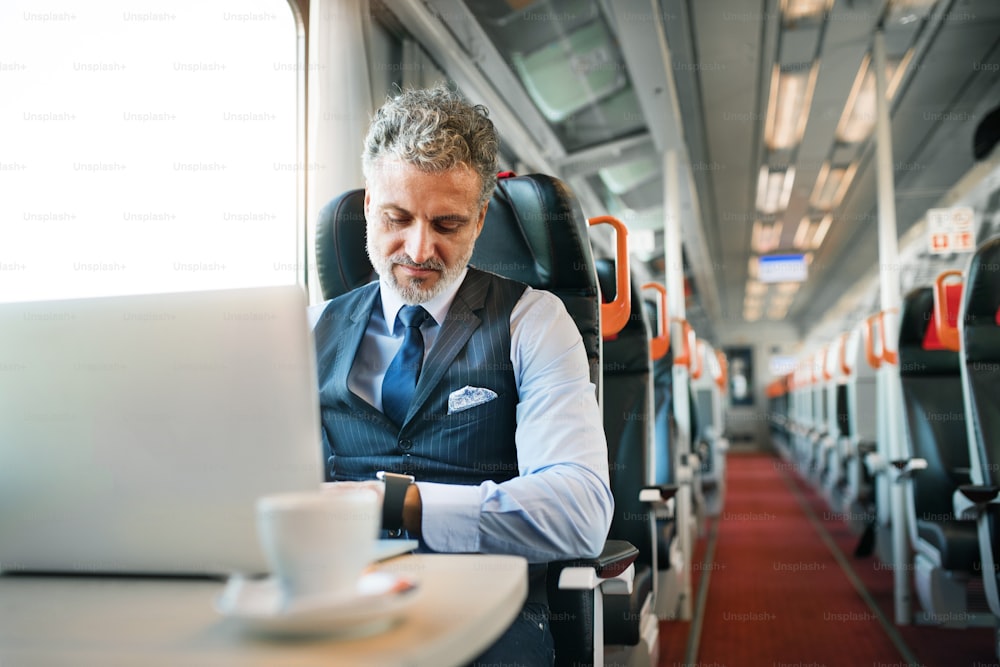 Gutaussehender reifer Geschäftsmann mit Laptop, der mit dem Zug reist. Ein Mann mit Smartwatch, der die Uhrzeit überprüft.