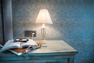 A lamp, a book and glasses on a bedside table in a hotel room.