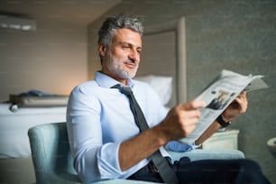 Homme d’affaires mûr et beau lisant des journaux dans une chambre d’hôtel.
