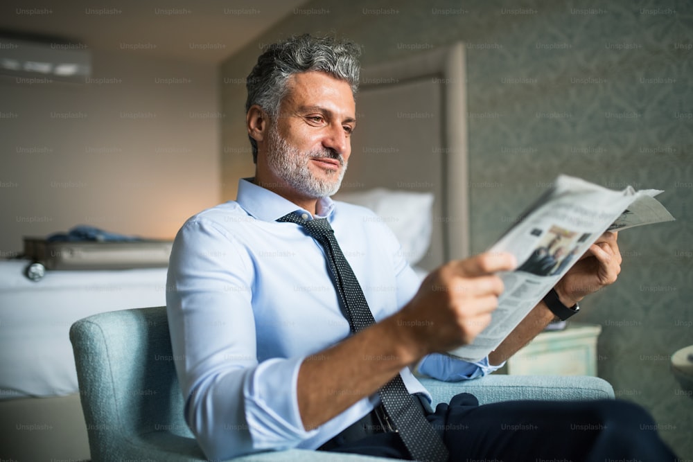 Mature, handsome businessman reading newspapers in a hotel room.