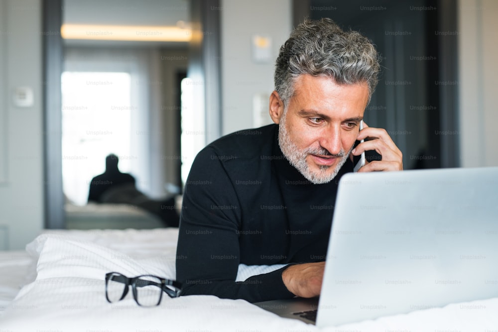 Mature businessman with laptop and smartphone in a hotel room. Handsome man working on computer and making a phone call.Mature businessman with smartphone in a hotel room. Handsome man making a phone call.