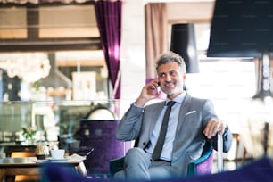 Handsome mature businessman with smartphone in a hotel lounge, making a phone call.