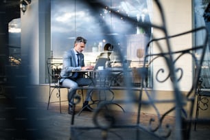 Homme d’affaires mature avec ordinateur portable assis dans un café d’hôtel en plein air.