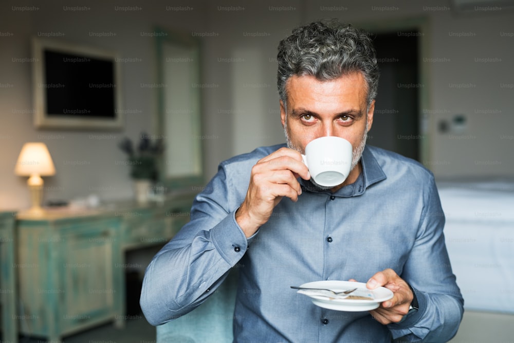 Empresário maduro e bonito bebendo café em um quarto de hotel.