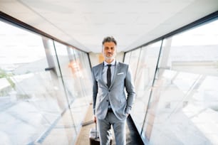 Mature businessman walking in the corridor with suitcase, travelling.