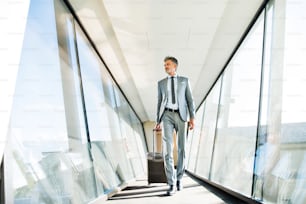 Uomo d'affari maturo che cammina nel corridoio con la valigia, viaggiando.