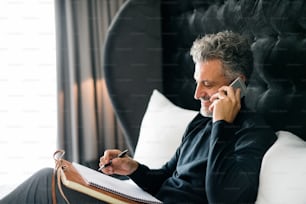 Mature businessman with smartphone in a hotel room. Handsome man making a phone call.