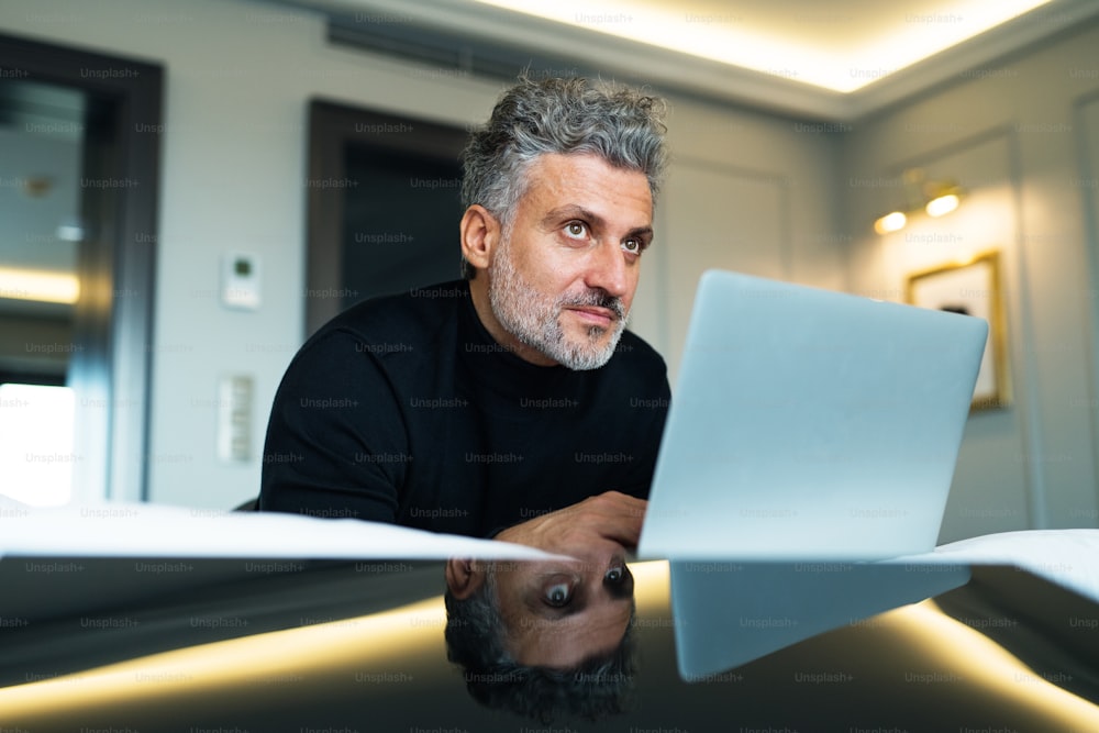 Homme d’affaires mature avec ordinateur portable dans une chambre d’hôtel. Bel homme travaillant sur ordinateur.