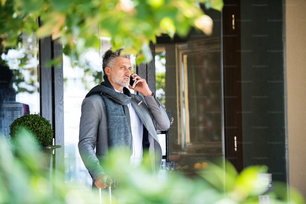 Handsome mature businessman with smartphone in front of a hotel, making a phone call.
