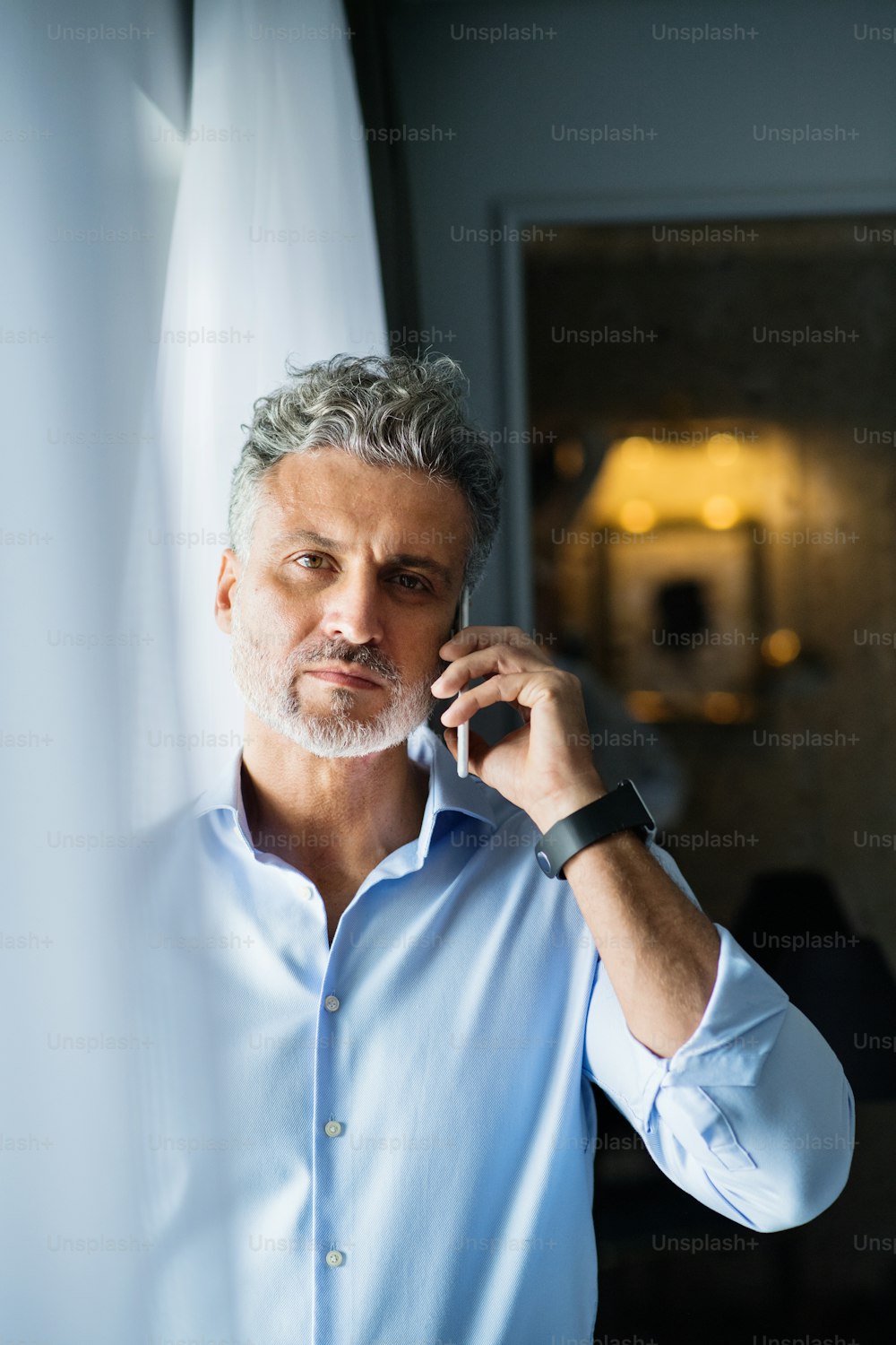 Mature businessman with smartphone in a hotel room. Handsome man standing at the window, making a phone call.