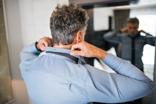 Mature businessman dressing up in a hotel room. Handsome man putting on a tie.