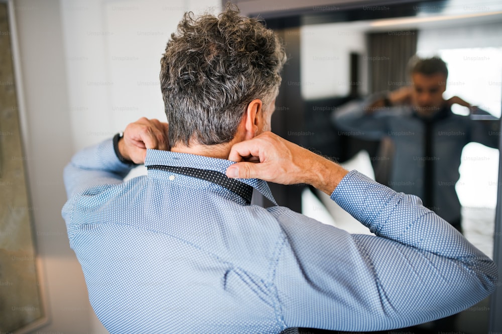 Mature businessman dressing up in a hotel room. Handsome man putting on a tie.