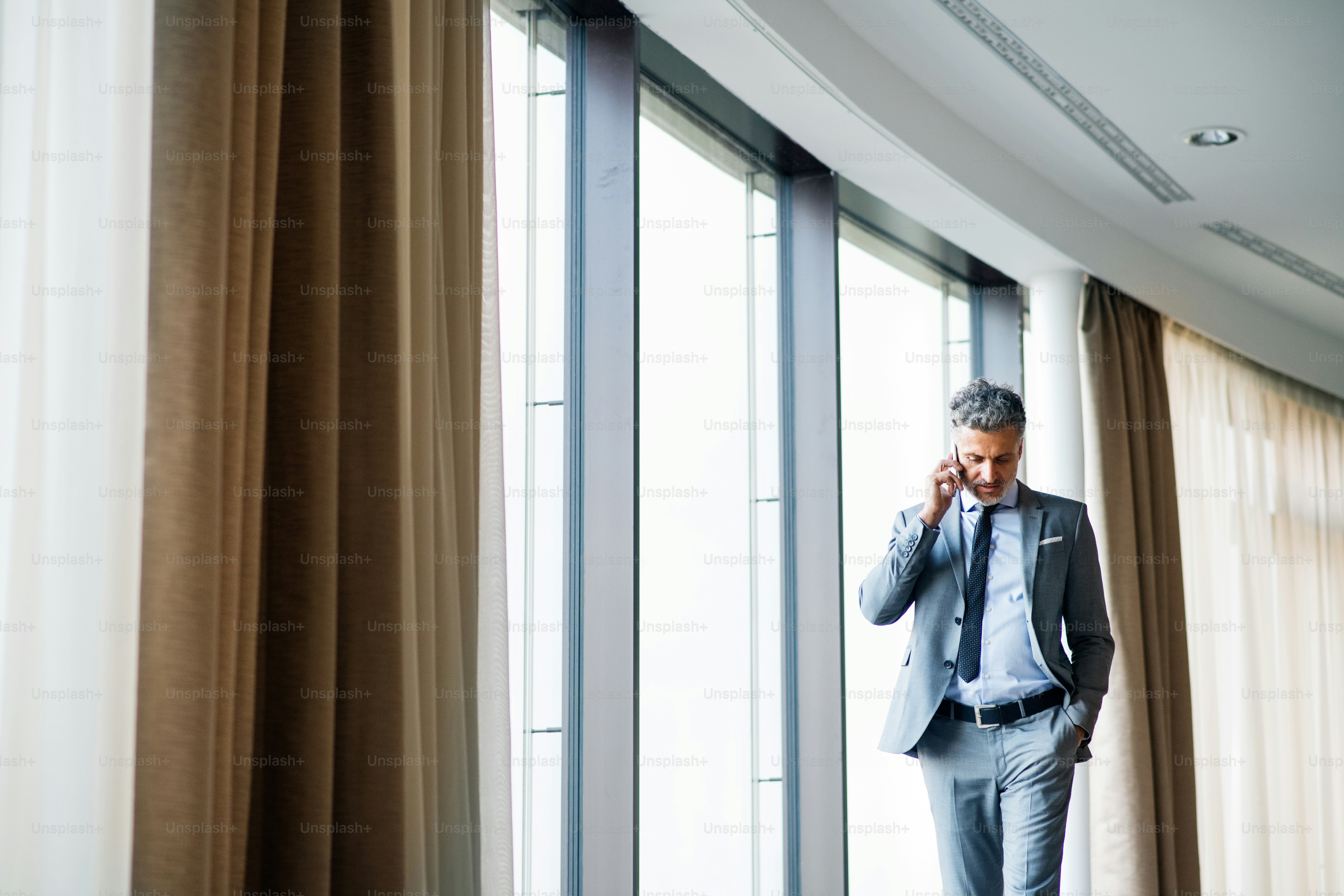 Uomo d'affari maturo in un hotel con uno smartphone. Uomo che fa una telefonata, camminando
