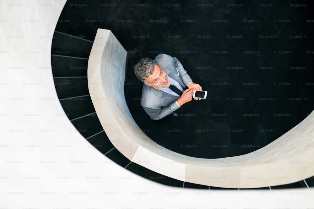 Hombre de negocios con teléfono inteligente parado en la parte inferior de la escalera, mirando hacia arriba. Vista superior.