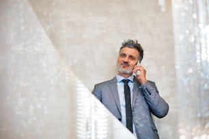 Reifer Geschäftsmann mit Smartphone, der sich an eine Betonwand lehnt und telefoniert.
