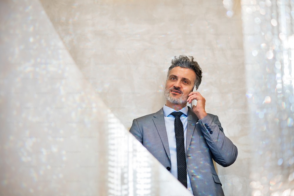 スマートフォンを持つ成熟した実業家がコンクリートの壁に寄りかかって電話をかける。