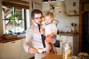 Young businessman coming home from work, holding his little son in the arms, drinking coffee.
