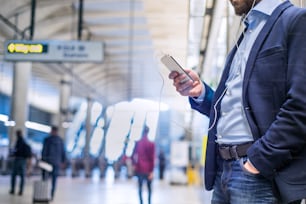 Primo piano di un uomo d'affari hipster irriconoscibile con lo smartphone in piedi sulla stazione della metropolitana che ascolta musica