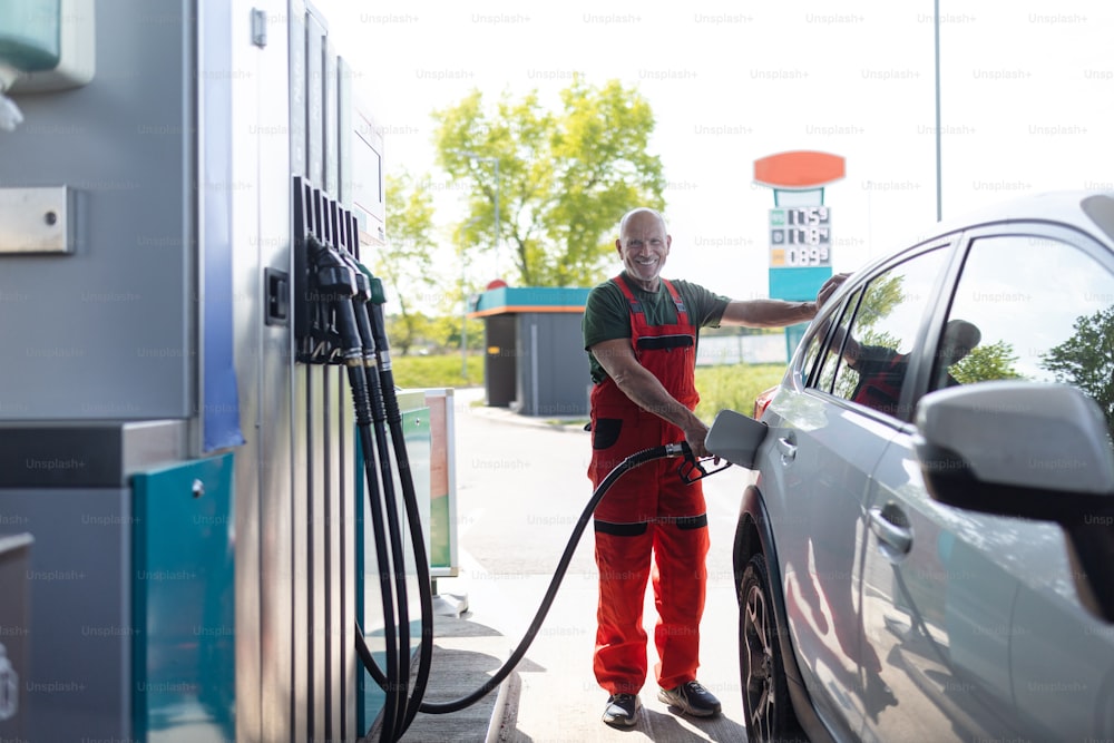 A senior worker standing on gas station and fueling car.