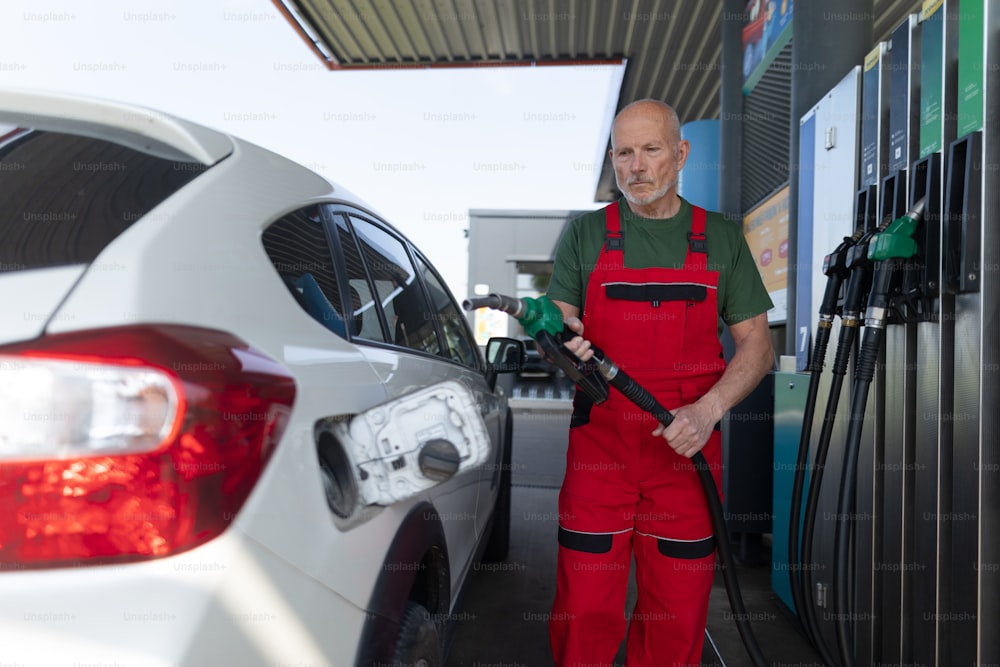 A senior worker standing on gas station and fueling car.