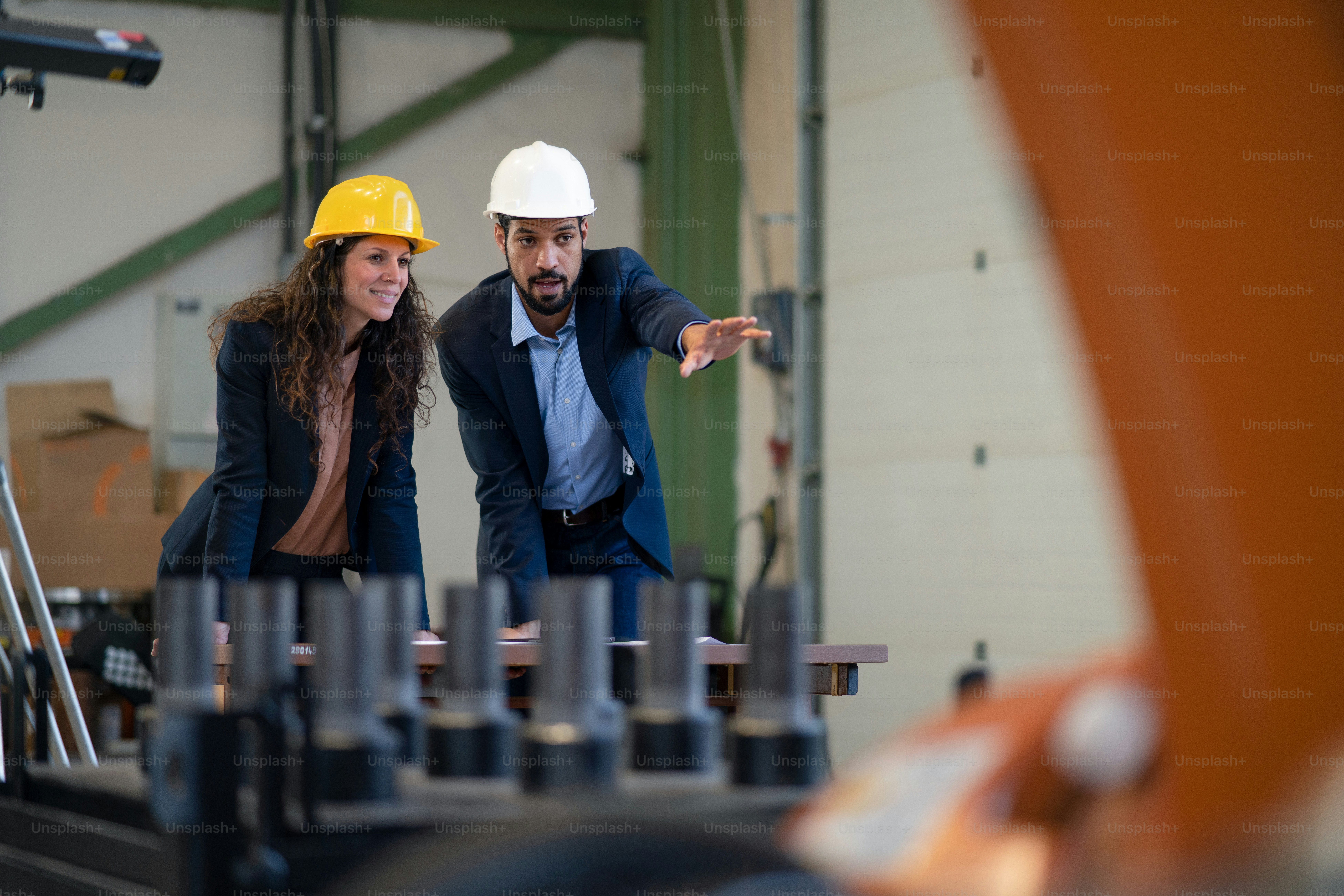 Ein Chefingenieur und Projektmanager in einer modernen Industriefabrik mit Roboterarmen, die über die Optimierung der Produktion sprechen und diese planen.