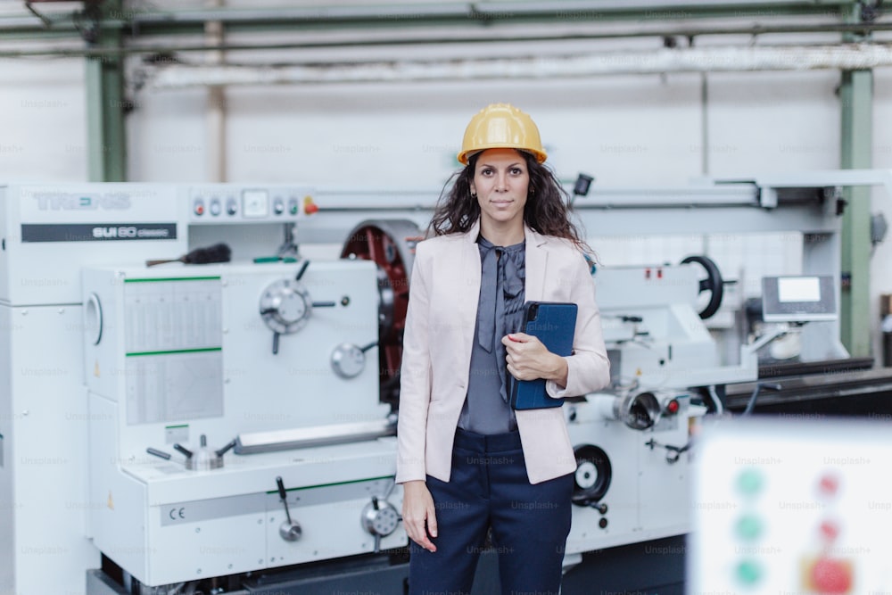 A portrait of female chief engineer in modern industrial factory using tablet and machine.