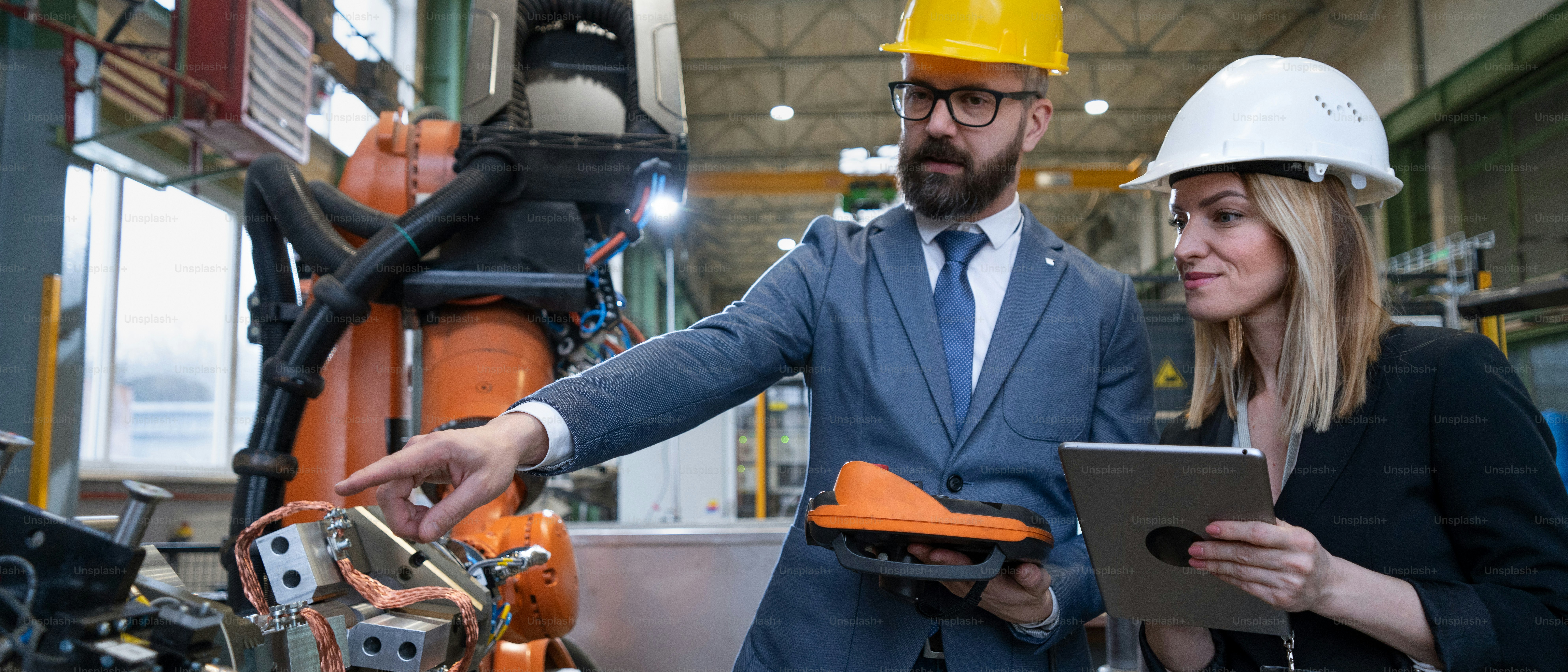 Un ingénieur en chef et chef de projet dans une usine industrielle moderne avec des bras robotiques parlant et planifiant l’optimisation de la production