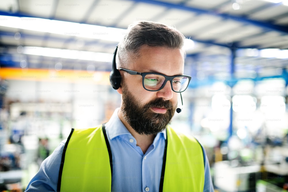 Front view of technician or engineer with headset standing in industrial factory, working.